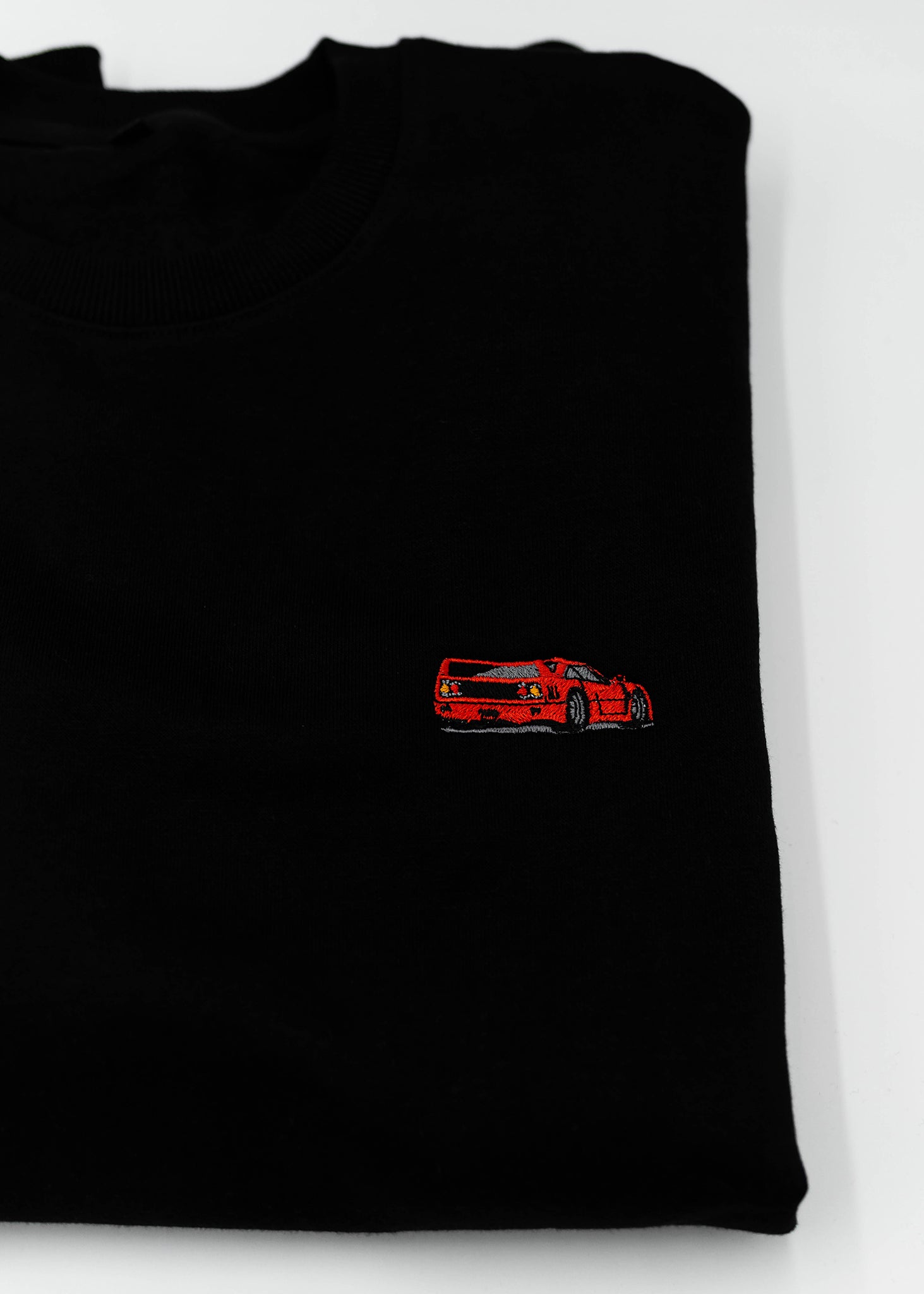 Close up of an embroidered F40 on a black men's high quality crewneck sweater. Photo shows the high quality detailed embroidery of a red F40. Fabric composition of the shirt is cotton and polyester. The material is very soft, stretchy, and non-transparent. The style of this sweater is a crewneck, long sleeve, elastic bottom, with embroidery on the left chest.