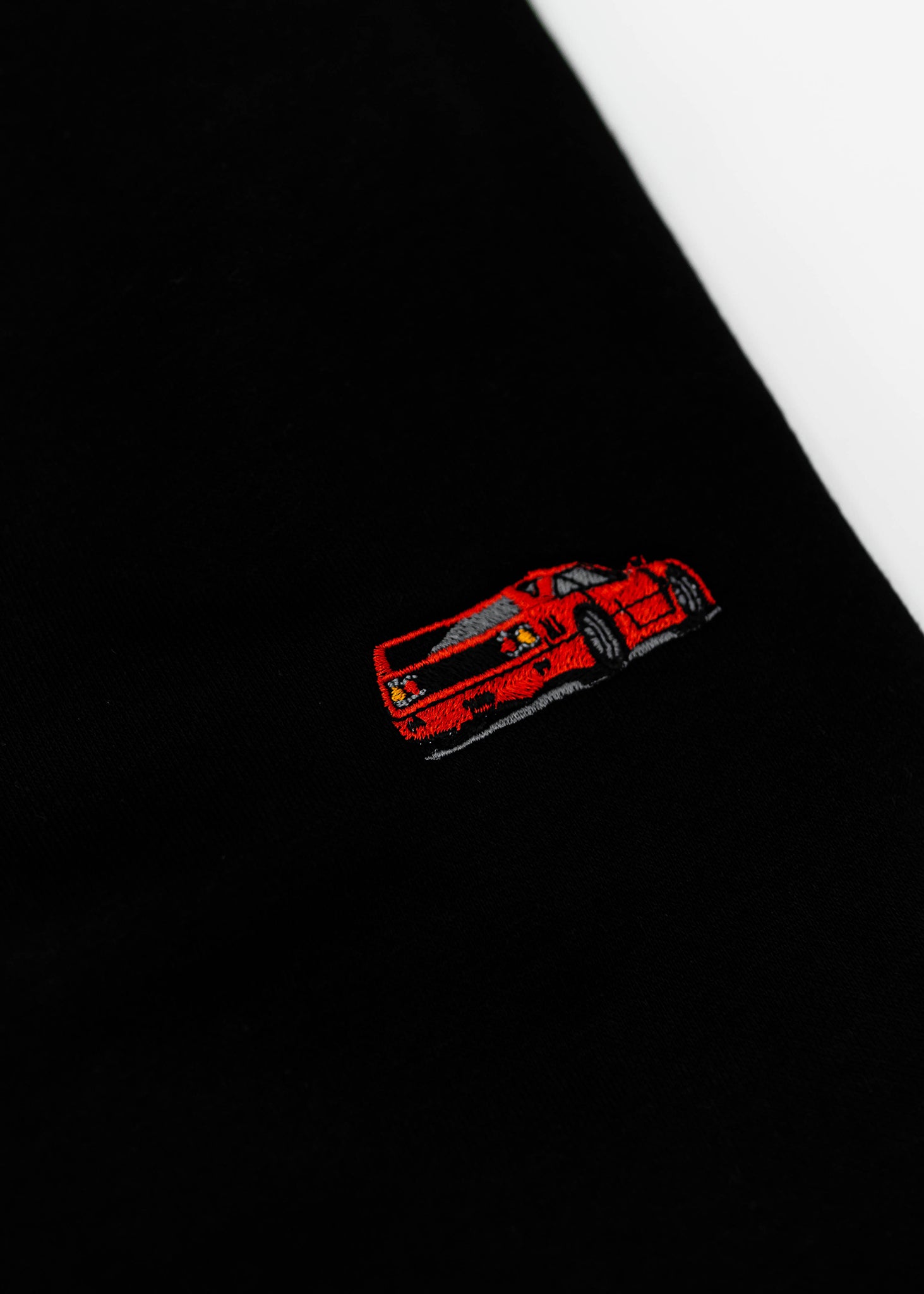 Close up of an embroidered F40 on a black men's high quality crewneck sweater. Photo shows the high quality detailed embroidery of a red F40. Fabric composition of the shirt is cotton and polyester. The material is very soft, stretchy, and non-transparent. The style of this sweater is a crewneck, long sleeve, elastic bottom, with embroidery on the left chest.