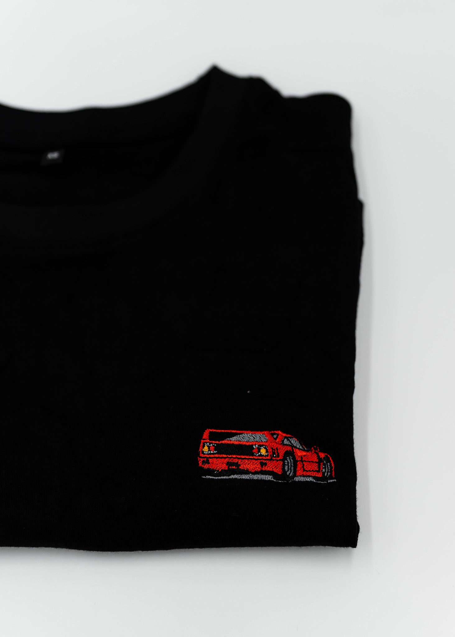 Close up of an embroidered F40 on a women's high quality cropped t-shirt. Photo shows the detailed embroidery of a red F40. Fabric composition of this tee is 100% cotton. The material is very soft, stretchy, and non-transparent. The style of this tshirt is a crewneck, short sleeve, cropped at the waist, with embroidery on the left chest.