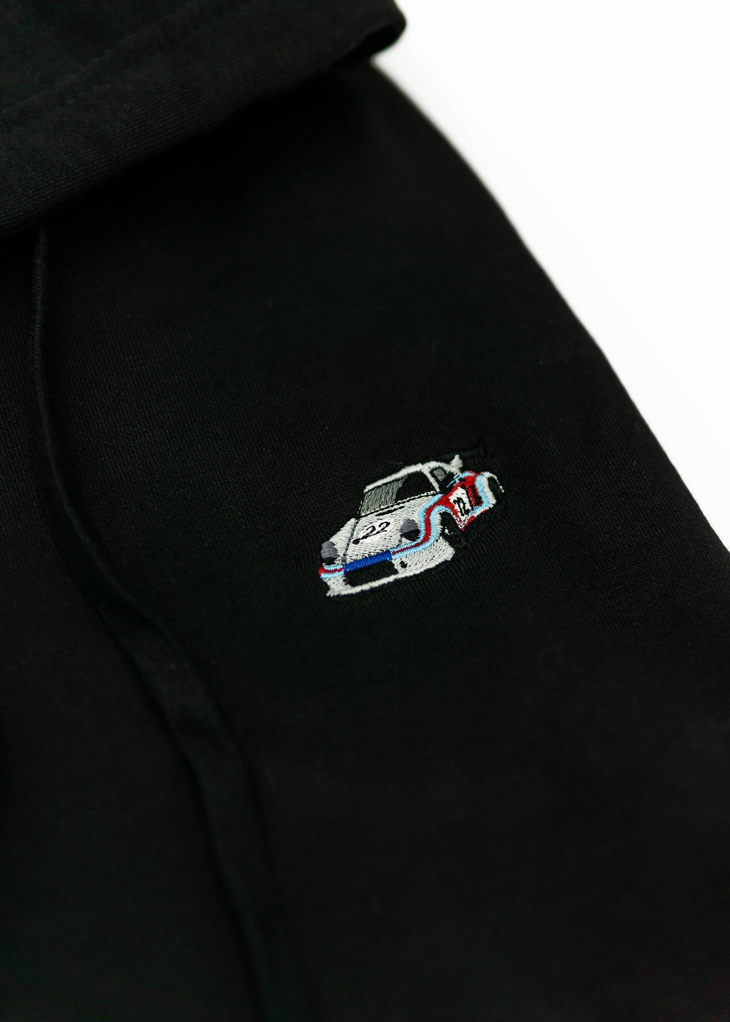 A black 911 RSR racing unisex hoodie for men and women. Photo is a close up view of the sweater with an embroidered Martini R13 911 RSR 2.1 Turbo. Fabric composition is cotton, polyester, and rayon. The material is very soft, stretchy, and non-transparent. The style of this hoodie is long sleeve, crewneck with a hood, hooded, with embroidery on the left chest.