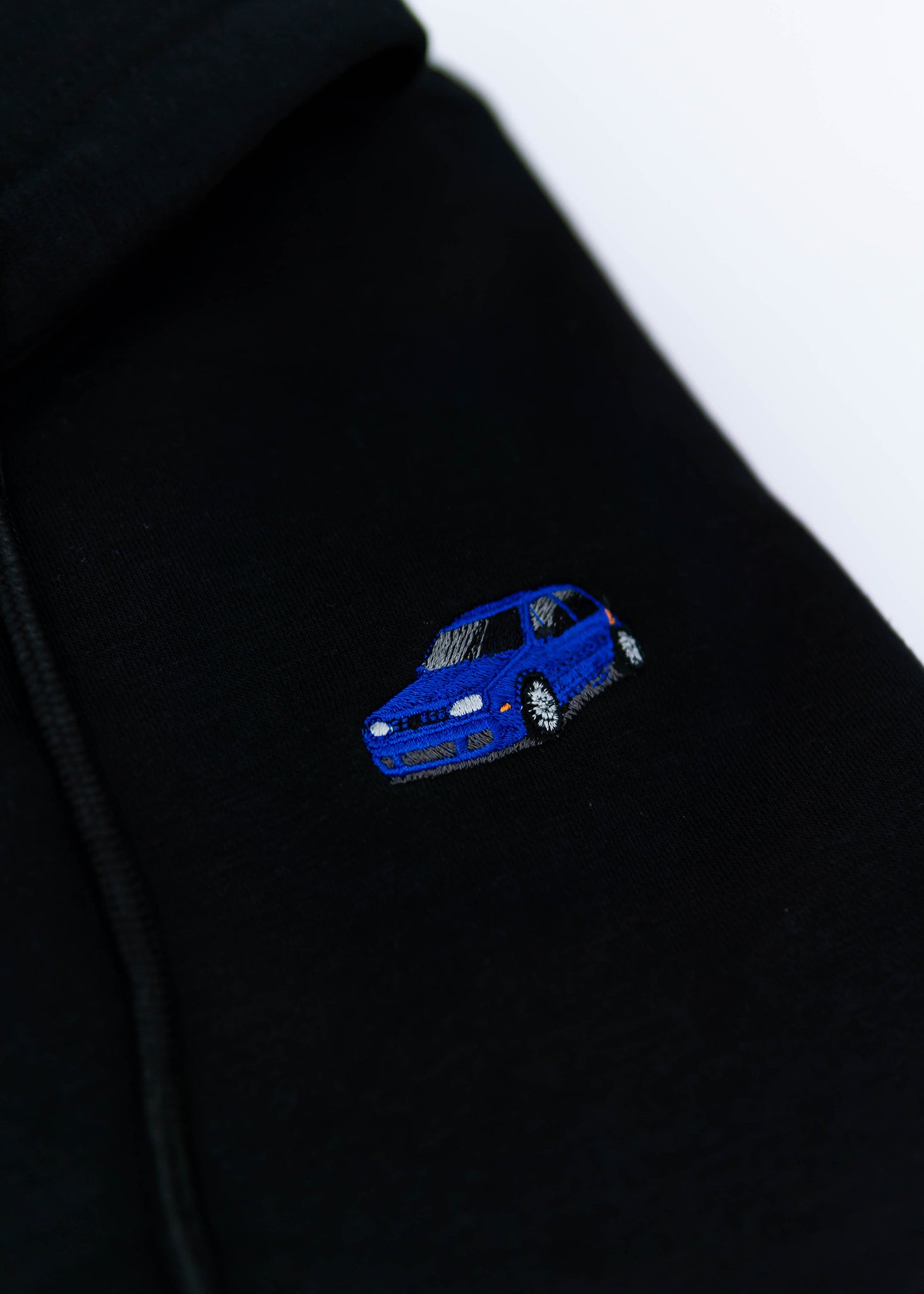 A black Mk4 Golf R32 cropped hoodie for women. Photo is a close up view of the cropped sweater with an embroidered blue Mk4 Golf R32. Fabric composition is cotton. The material is soft, stretchy, and non-transparent. The style of this crop hoodie is long sleeve, crewneck with a hood, hooded, with embroidery on the chest.