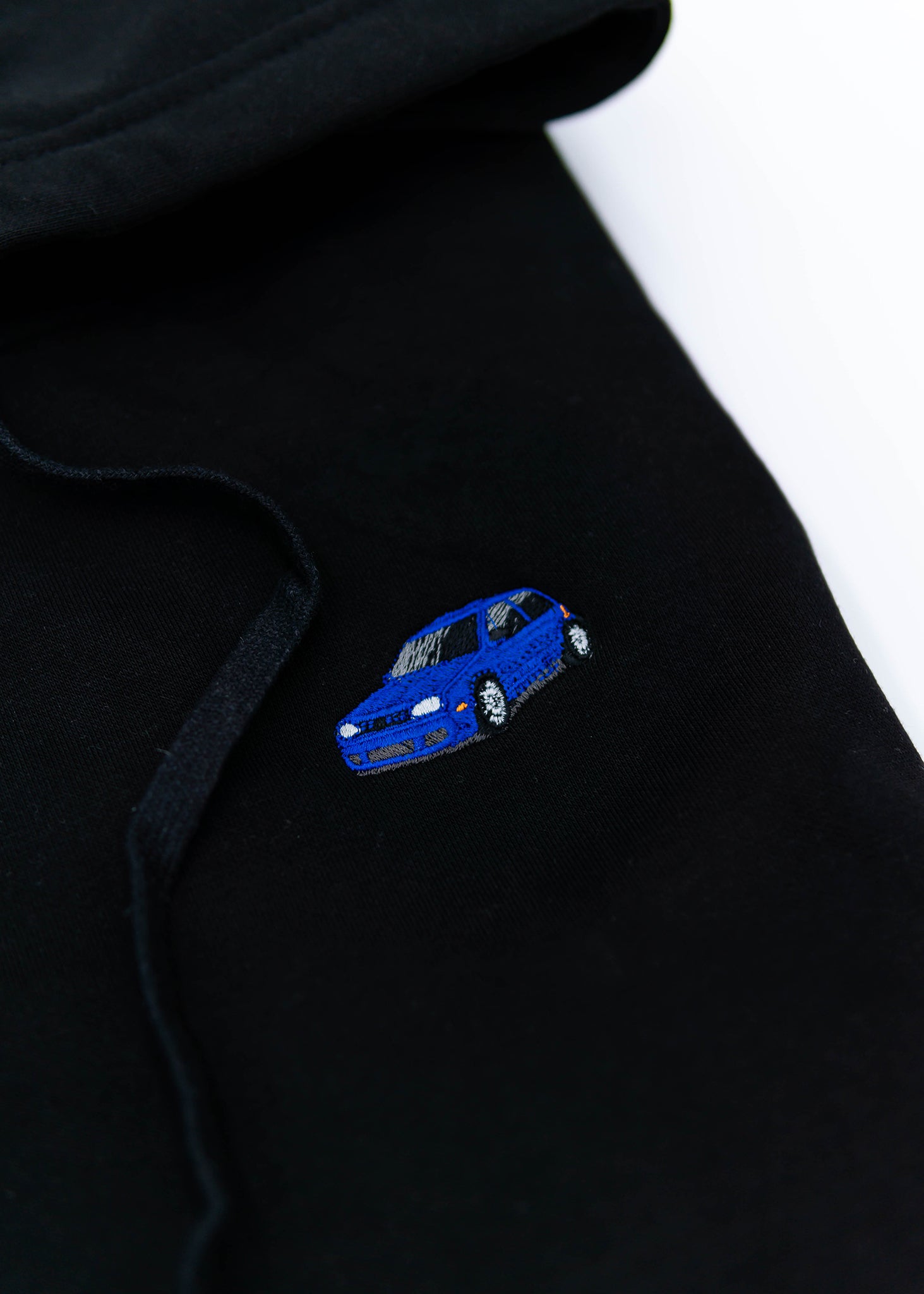 A black Mk4 Golf R32 unisex hoodie for men and women. Photo is a close up view of the sweater with an embroidered blue Mk4 Golf R32. Fabric composition is cotton, polyester, and rayon. The material is very soft, stretchy, and non-transparent. The style of this hoodie is long sleeve, crewneck with a hood, hooded, with embroidery on the left chest.