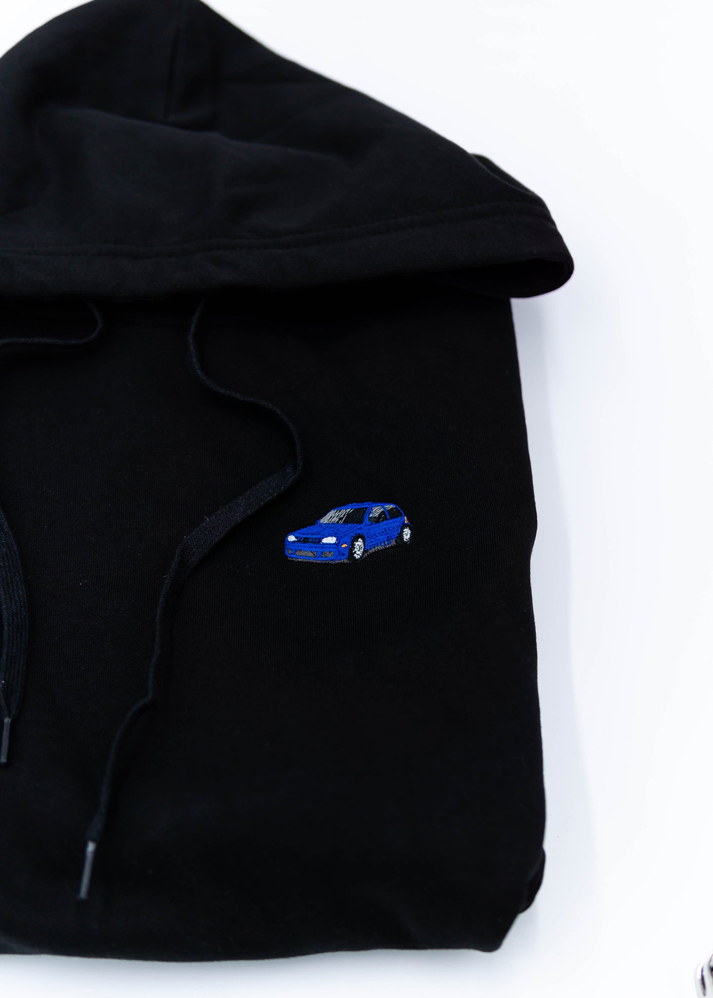 A black Mk4 Golf R32 unisex hoodie for men and women. Photo is a close up view of the sweater with an embroidered blue Mk4 Golf R32. Fabric composition is cotton, polyester, and rayon. The material is very soft, stretchy, and non-transparent. The style of this hoodie is long sleeve, crewneck with a hood, hooded, with embroidery on the left chest.